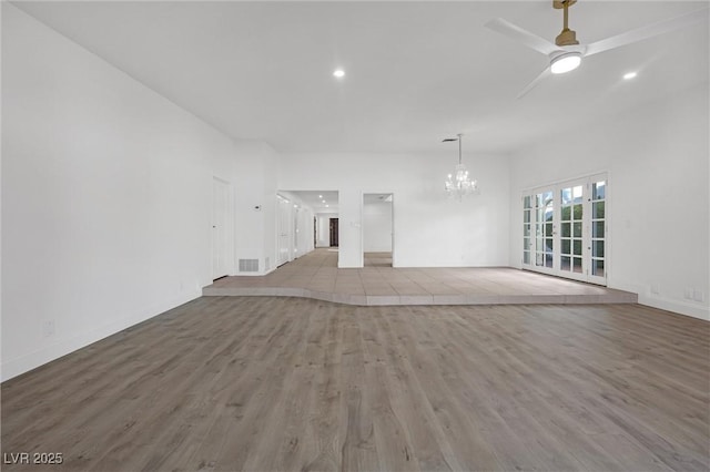 unfurnished living room with ceiling fan with notable chandelier and light hardwood / wood-style flooring