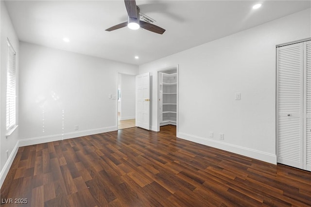 unfurnished bedroom with dark wood-type flooring, a spacious closet, and ceiling fan