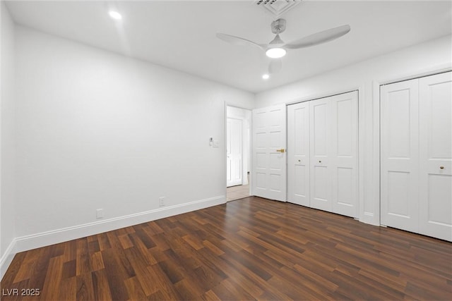 unfurnished bedroom featuring ceiling fan, dark wood-type flooring, and multiple closets