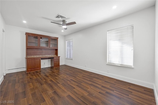 unfurnished office featuring dark wood-type flooring, a baseboard heating unit, ceiling fan, and built in desk