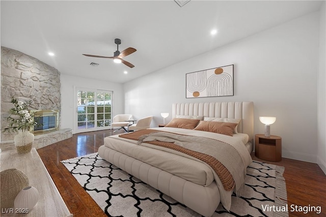 bedroom with ceiling fan, dark hardwood / wood-style flooring, and a stone fireplace