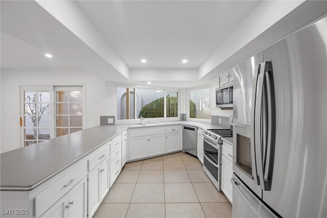 kitchen with light tile patterned floors, white cabinets, kitchen peninsula, stainless steel appliances, and a tray ceiling