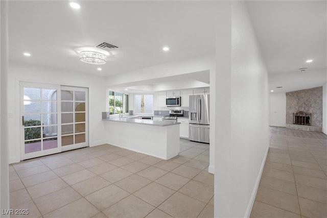 kitchen with a stone fireplace, appliances with stainless steel finishes, white cabinetry, light tile patterned floors, and kitchen peninsula