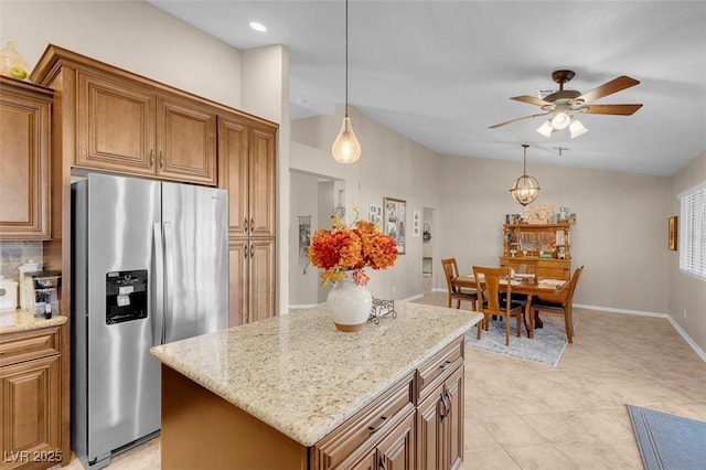 kitchen featuring a center island, backsplash, hanging light fixtures, stainless steel fridge, and light stone counters