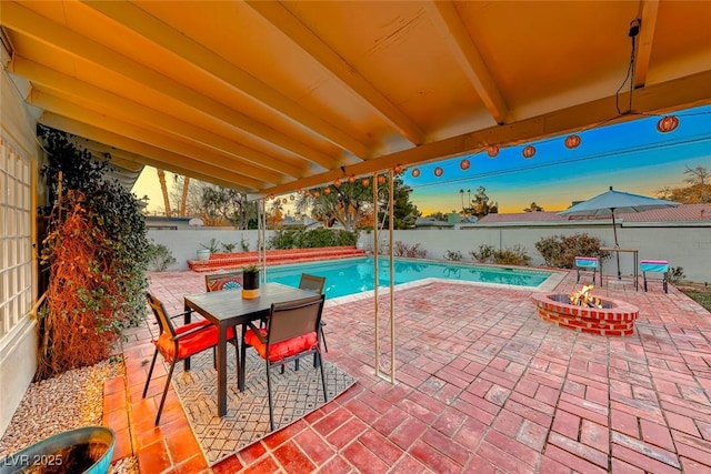 pool at dusk with an outdoor fire pit and a patio