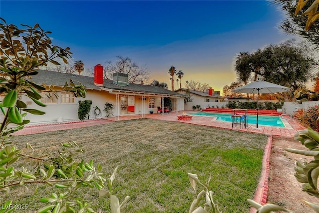 back house at dusk featuring a fenced in pool, a patio area, and a lawn