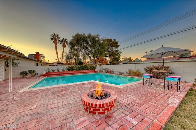 pool at dusk with a fire pit and a patio area