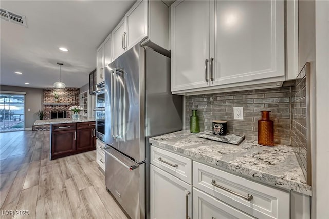 kitchen with white cabinetry, stainless steel appliances, tasteful backsplash, and light wood-type flooring