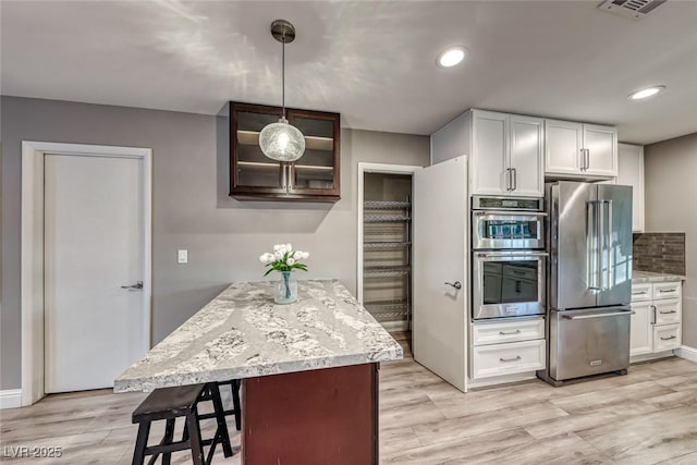 kitchen featuring decorative light fixtures, white cabinets, backsplash, stainless steel appliances, and light wood-type flooring