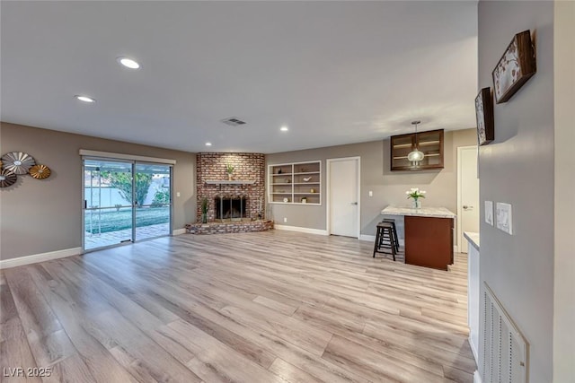 unfurnished living room featuring built in shelves, a fireplace, and light hardwood / wood-style floors