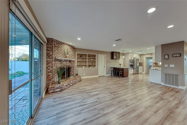 unfurnished living room with a fireplace, light hardwood / wood-style floors, and built in shelves