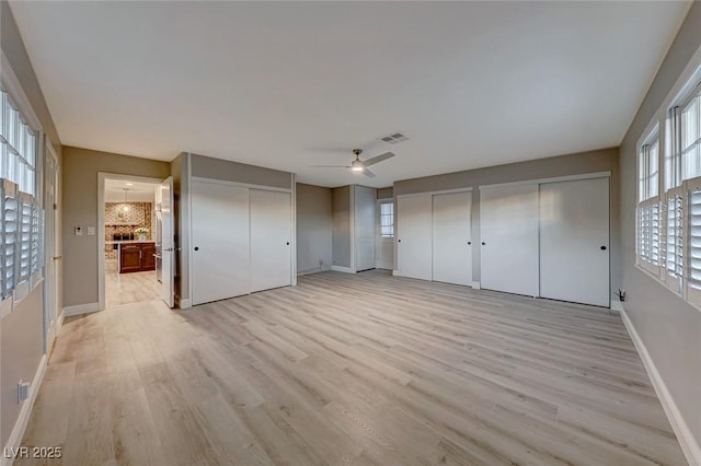 unfurnished bedroom featuring multiple closets, ensuite bathroom, ceiling fan, and light wood-type flooring