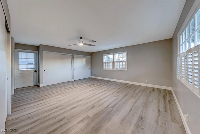 unfurnished bedroom with ceiling fan, light hardwood / wood-style flooring, and multiple closets