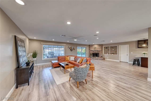 living room with a brick fireplace, built in features, ceiling fan, and light hardwood / wood-style flooring