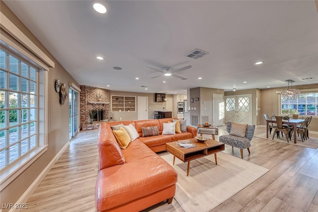 living room featuring ceiling fan with notable chandelier, a fireplace, and light wood-type flooring