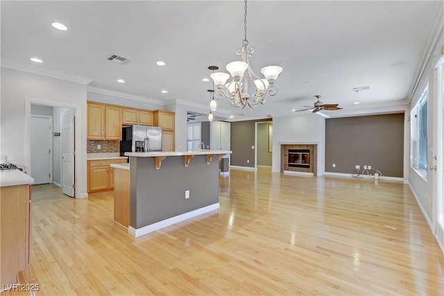 kitchen featuring light brown cabinets, hanging light fixtures, backsplash, stainless steel fridge with ice dispenser, and a kitchen island