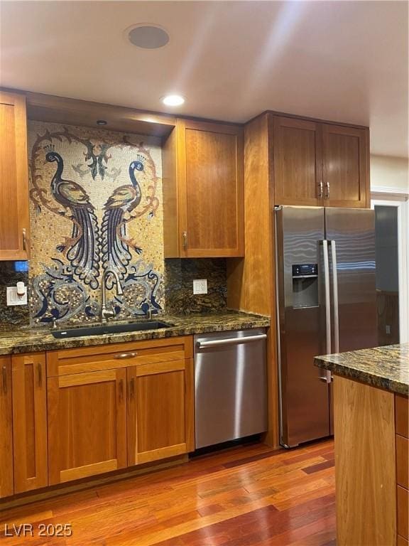 kitchen featuring appliances with stainless steel finishes, dark stone countertops, decorative backsplash, sink, and light hardwood / wood-style flooring