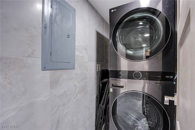 laundry area featuring stacked washer / dryer, tile walls, and electric panel