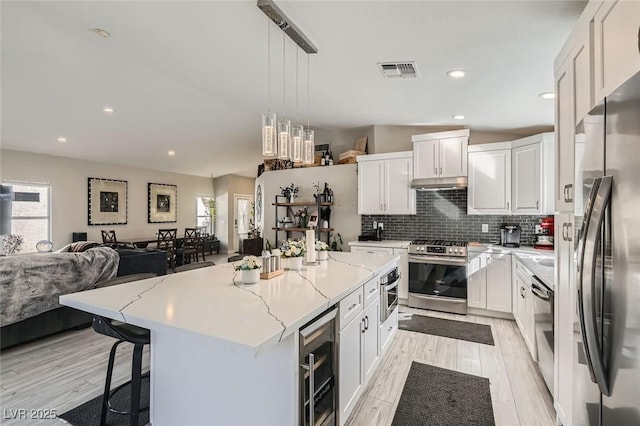 kitchen featuring a kitchen island, appliances with stainless steel finishes, pendant lighting, white cabinets, and beverage cooler