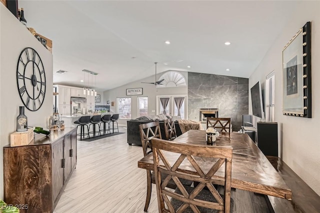 dining space with lofted ceiling, light hardwood / wood-style floors, a premium fireplace, and ceiling fan