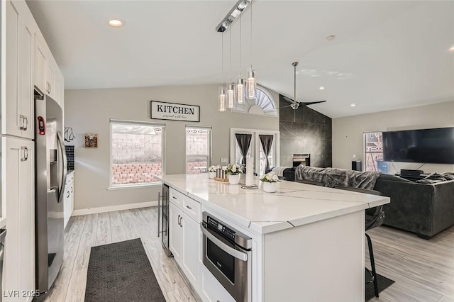 kitchen with vaulted ceiling, appliances with stainless steel finishes, white cabinetry, hanging light fixtures, and a center island with sink