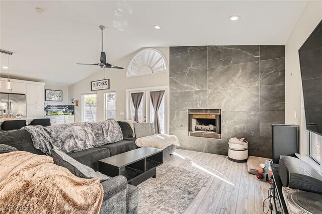 living room with tile walls, lofted ceiling, recessed lighting, a tiled fireplace, and wood finished floors