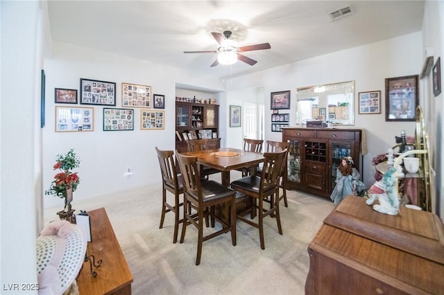 dining area with ceiling fan and light colored carpet