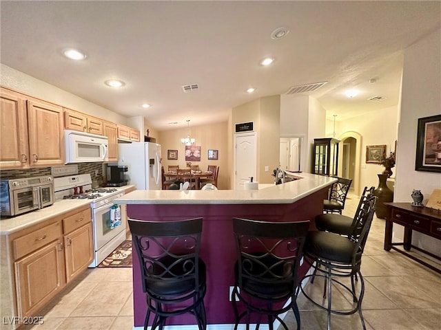 kitchen with white appliances, an island with sink, a kitchen bar, and light brown cabinetry