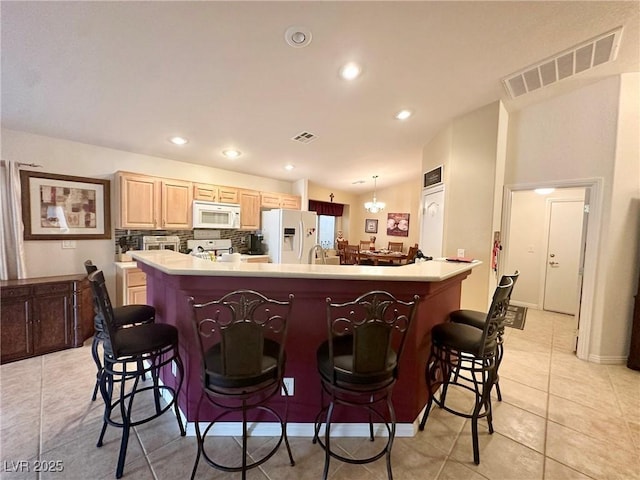 kitchen featuring white appliances, a kitchen island, light brown cabinets, and a kitchen breakfast bar