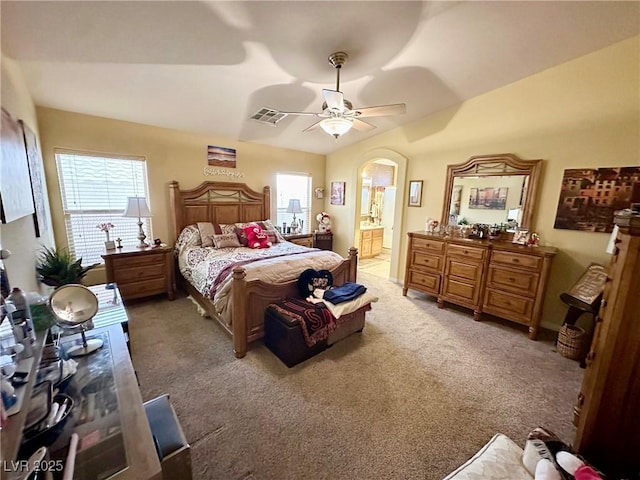 bedroom with vaulted ceiling, light colored carpet, ceiling fan, and ensuite bath