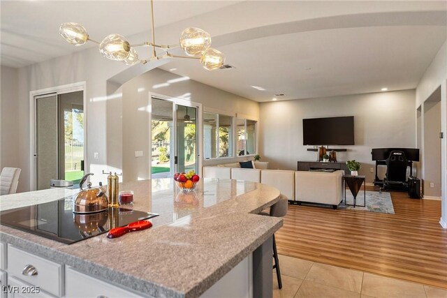 kitchen with light stone counters, black electric stovetop, white cabinets, light tile patterned flooring, and decorative light fixtures