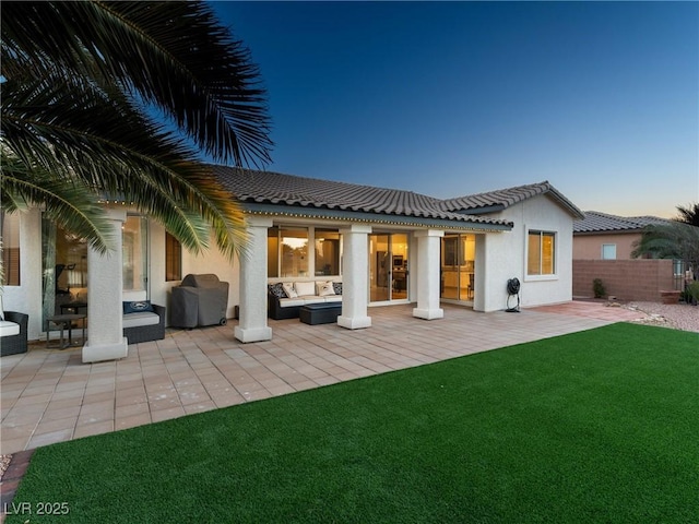 back house at dusk featuring a patio, an outdoor hangout area, and a lawn