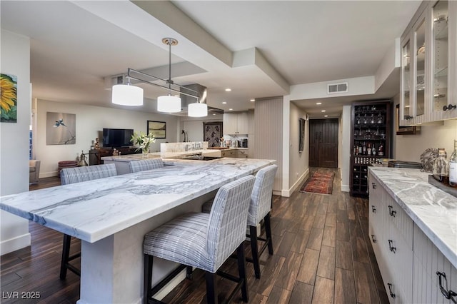 kitchen with light stone countertops, a kitchen bar, decorative light fixtures, dark wood-type flooring, and a large island