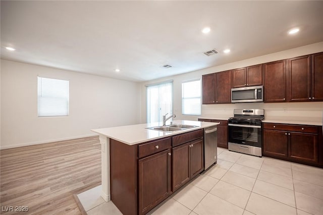 kitchen featuring light hardwood / wood-style flooring, appliances with stainless steel finishes, sink, a kitchen island with sink, and dark brown cabinetry