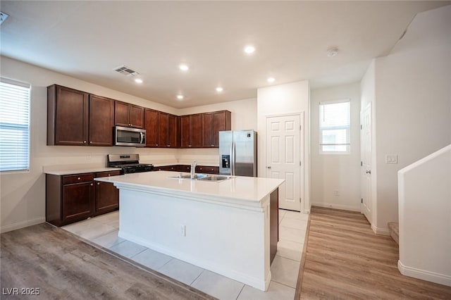 kitchen with dark brown cabinets, appliances with stainless steel finishes, sink, light tile patterned floors, and an island with sink