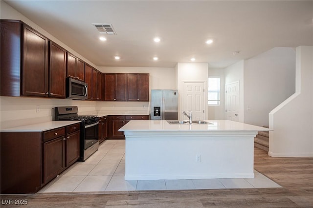 kitchen with a kitchen island with sink, light tile patterned floors, sink, dark brown cabinetry, and stainless steel appliances