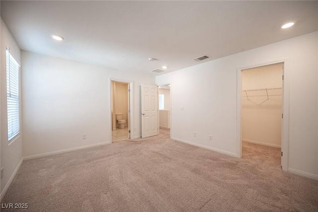 unfurnished bedroom with a spacious closet, ensuite bathroom, a closet, and light carpet