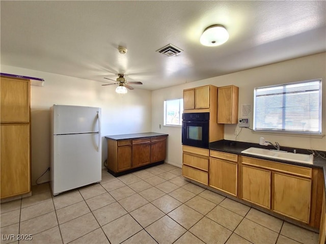 kitchen featuring light tile patterned floors, sink, black oven, ceiling fan, and white refrigerator