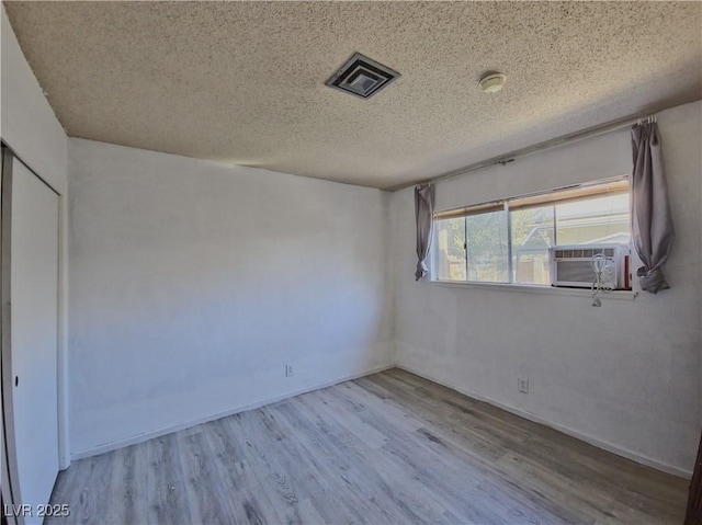 spare room featuring a textured ceiling, light hardwood / wood-style flooring, and cooling unit