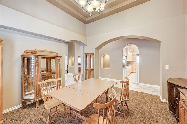 carpeted dining room featuring a towering ceiling, a raised ceiling, and an inviting chandelier