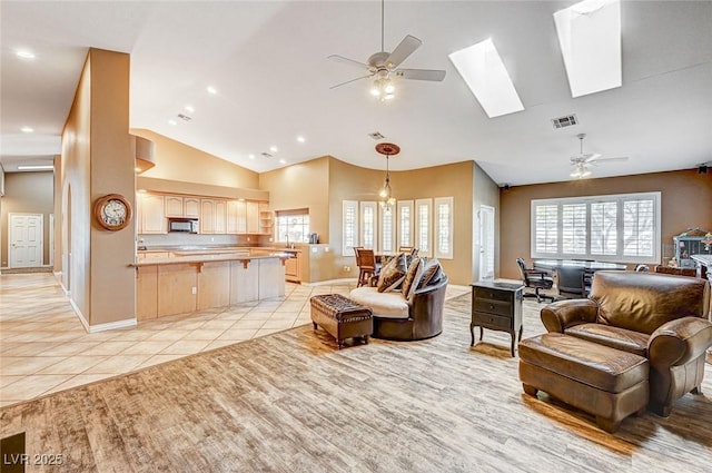 living room featuring ceiling fan, high vaulted ceiling, a skylight, and light tile patterned floors