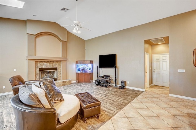 living room with ceiling fan, lofted ceiling with skylight, light tile patterned floors, and a fireplace