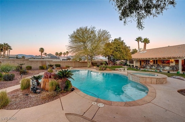 pool at dusk featuring an in ground hot tub and a patio area