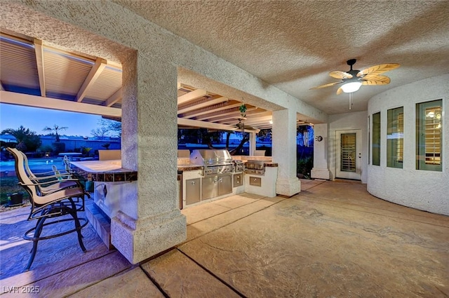 patio terrace at dusk featuring ceiling fan, a bar, and area for grilling