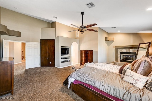 carpeted bedroom featuring ceiling fan, a high ceiling, and a tile fireplace