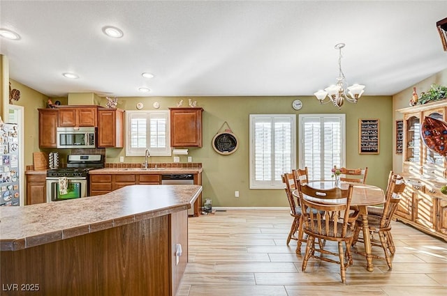 kitchen with appliances with stainless steel finishes, sink, decorative light fixtures, light wood-type flooring, and an inviting chandelier