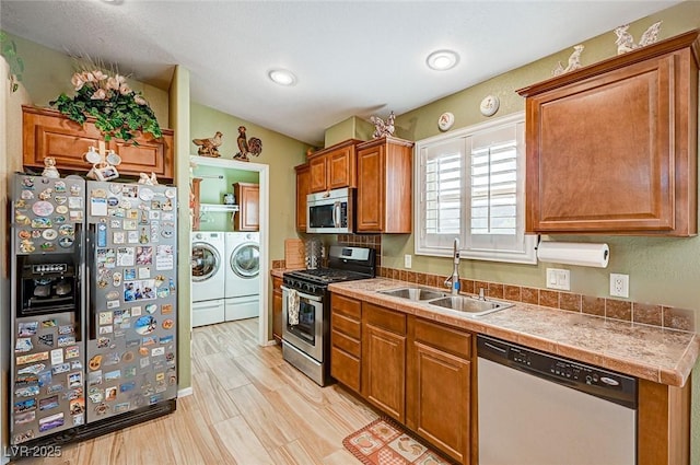 kitchen with sink, light hardwood / wood-style floors, washer and clothes dryer, and appliances with stainless steel finishes