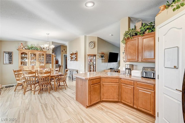 kitchen with pendant lighting, lofted ceiling, light hardwood / wood-style floors, kitchen peninsula, and a notable chandelier