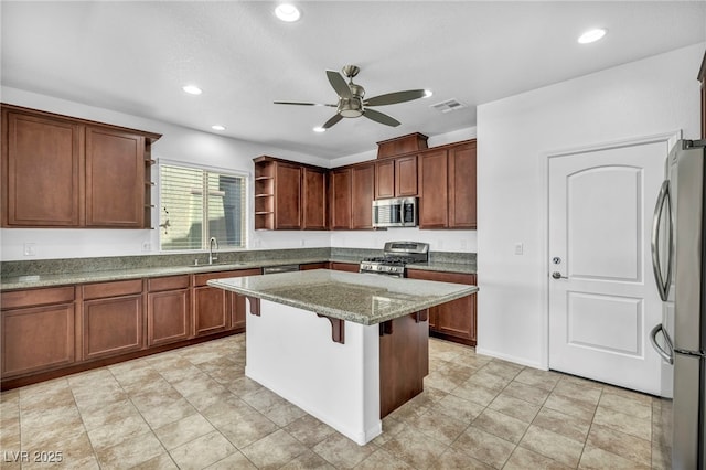 kitchen with ceiling fan, appliances with stainless steel finishes, sink, dark stone counters, and a center island