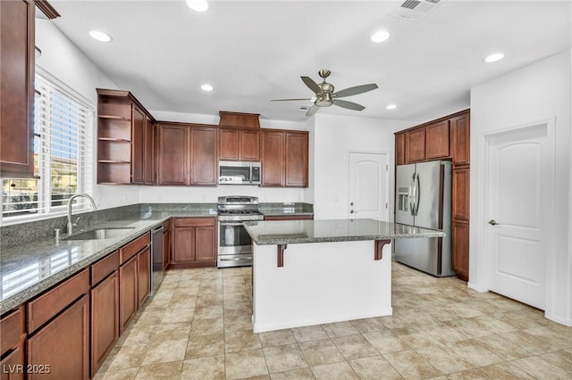 kitchen with appliances with stainless steel finishes, dark stone countertops, sink, a kitchen breakfast bar, and ceiling fan